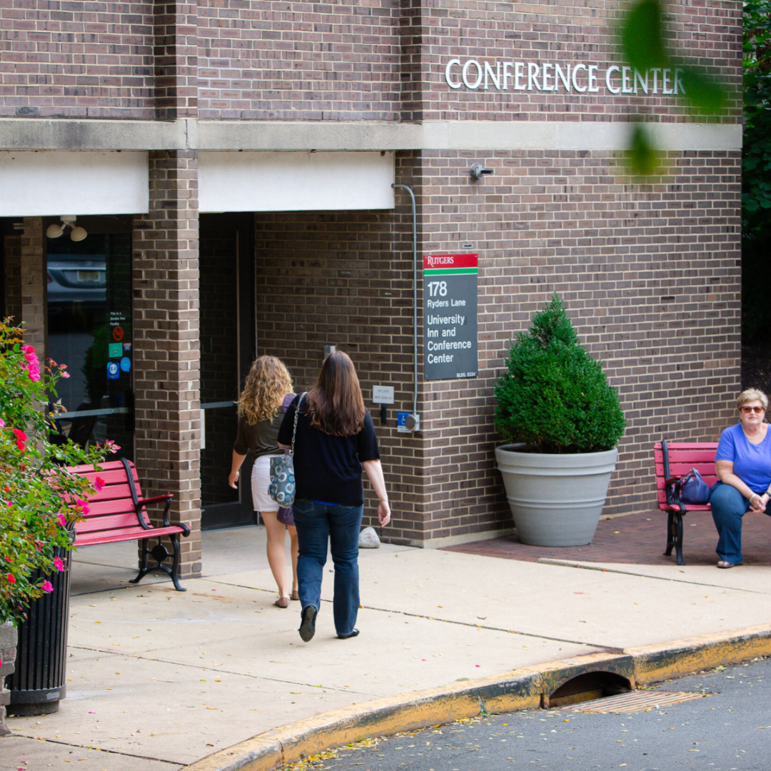 enterance of the rutgers inn and conference center with two people walking in and another visitor sitting on nearby red bench