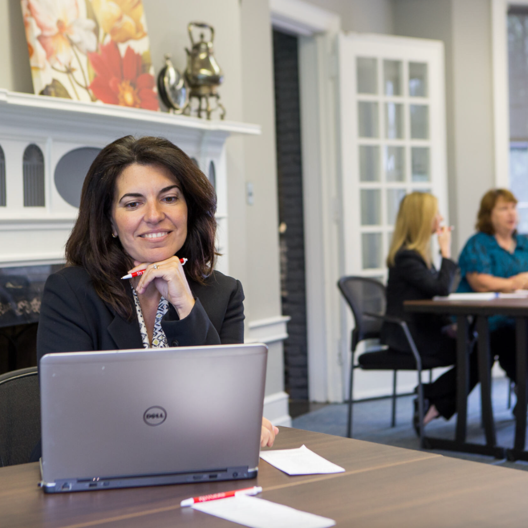 meeting in progress with woman looking at her computer and people chatting in the background